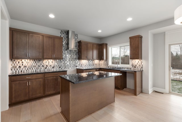 kitchen with dark stone countertops, a kitchen island, a healthy amount of sunlight, and wall chimney range hood