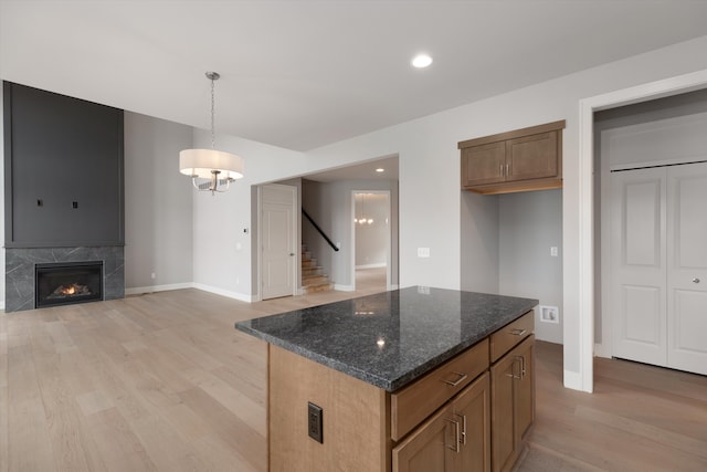 kitchen with pendant lighting, a center island, dark stone counters, light hardwood / wood-style floors, and a tiled fireplace