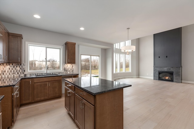 kitchen with a center island, sink, light hardwood / wood-style flooring, dark stone countertops, and a fireplace