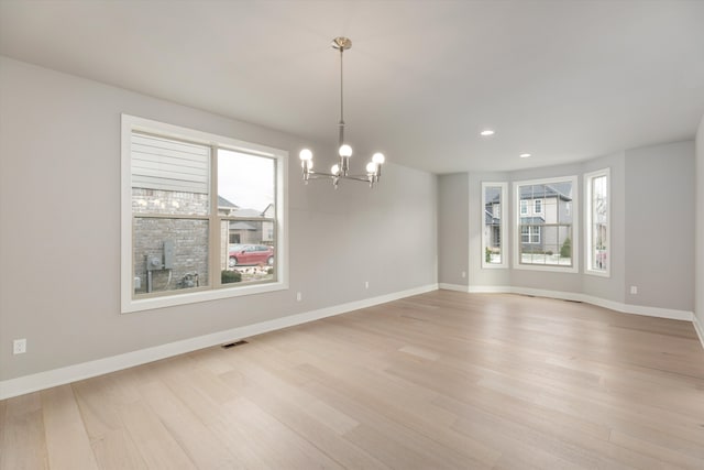 spare room with light hardwood / wood-style floors and an inviting chandelier