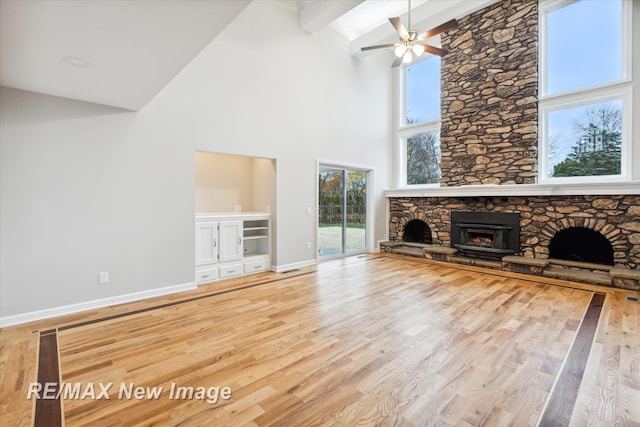 unfurnished living room featuring hardwood / wood-style flooring, beam ceiling, a fireplace, and high vaulted ceiling