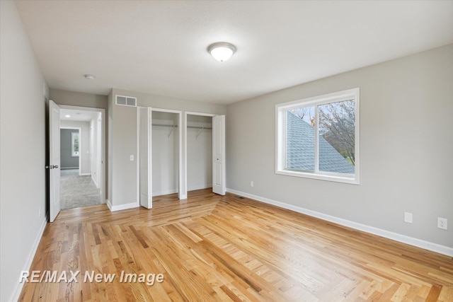 unfurnished bedroom featuring hardwood / wood-style floors and multiple closets