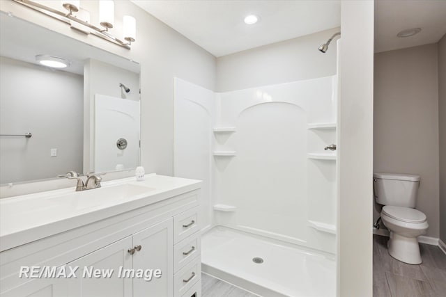 bathroom with a shower, hardwood / wood-style floors, vanity, and toilet