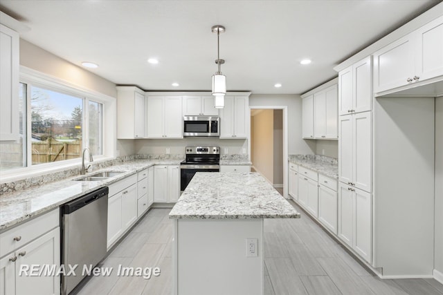 kitchen with pendant lighting, white cabinets, sink, appliances with stainless steel finishes, and a kitchen island