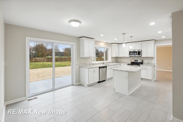 kitchen featuring light stone countertops, appliances with stainless steel finishes, decorative light fixtures, white cabinets, and a center island