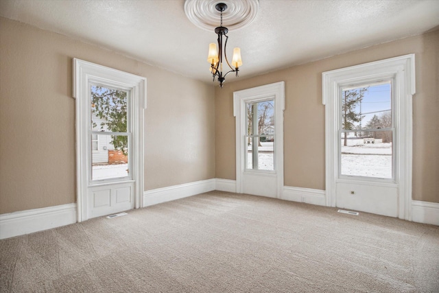 unfurnished room with carpet flooring, plenty of natural light, a textured ceiling, and an inviting chandelier