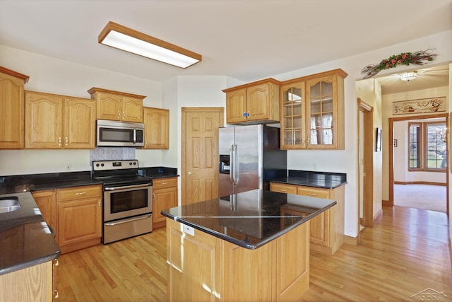 kitchen featuring a center island, stainless steel appliances, a kitchen breakfast bar, dark stone countertops, and light hardwood / wood-style floors