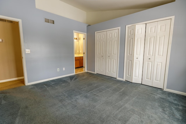 unfurnished bedroom featuring visible vents, two closets, dark carpet, baseboards, and vaulted ceiling