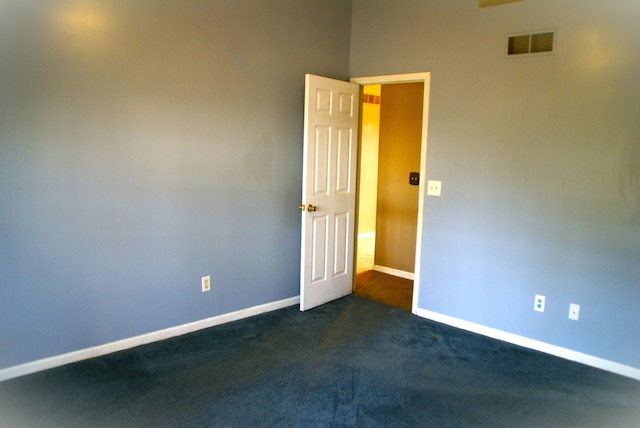 empty room with visible vents, dark carpet, and baseboards