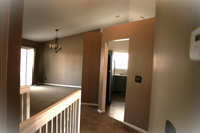 hall featuring baseboards, a chandelier, and dark carpet