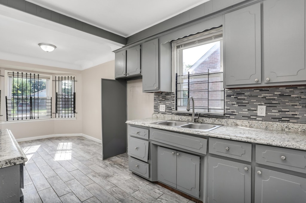 kitchen with decorative backsplash, light wood-type flooring, gray cabinetry, and sink