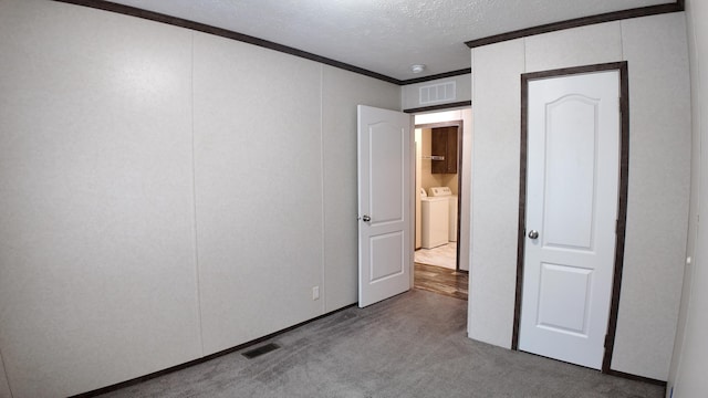 carpeted empty room with a textured ceiling, washing machine and dryer, and crown molding