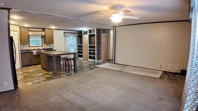 kitchen featuring a kitchen breakfast bar, ceiling fan, ornamental molding, a textured ceiling, and a kitchen island