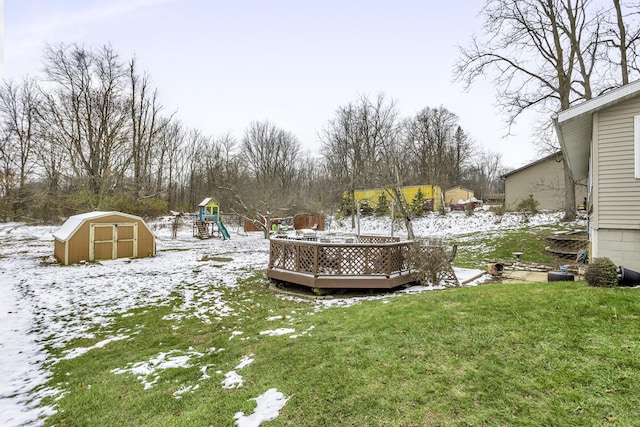 yard layered in snow with a playground, a deck, and a storage unit