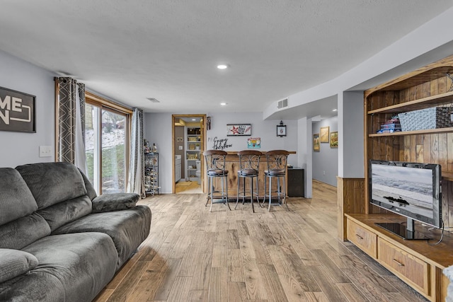 living room featuring a textured ceiling, light hardwood / wood-style floors, and bar