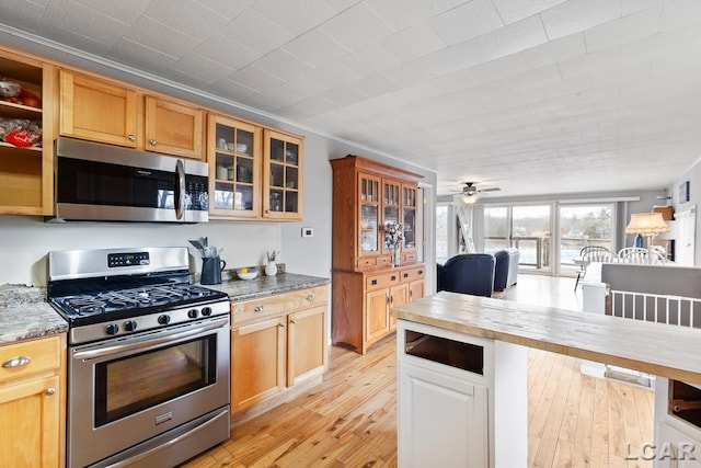 kitchen featuring appliances with stainless steel finishes, light wood-type flooring, dark stone counters, ceiling fan, and crown molding