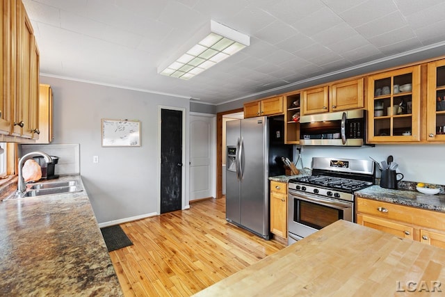 kitchen featuring sink, dark stone counters, light hardwood / wood-style floors, appliances with stainless steel finishes, and ornamental molding