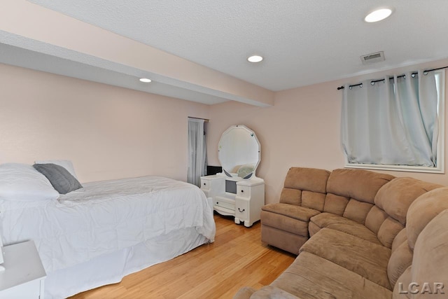 bedroom featuring beamed ceiling, light hardwood / wood-style floors, and a textured ceiling