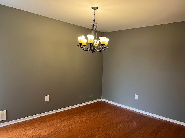 spare room with hardwood / wood-style flooring and a notable chandelier