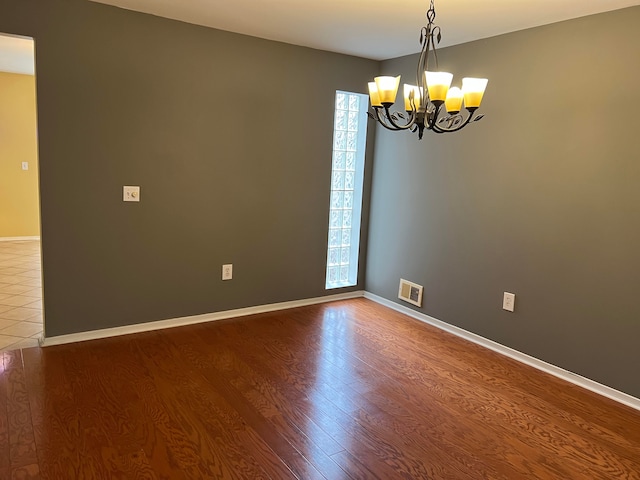 empty room with hardwood / wood-style floors, a healthy amount of sunlight, and a notable chandelier