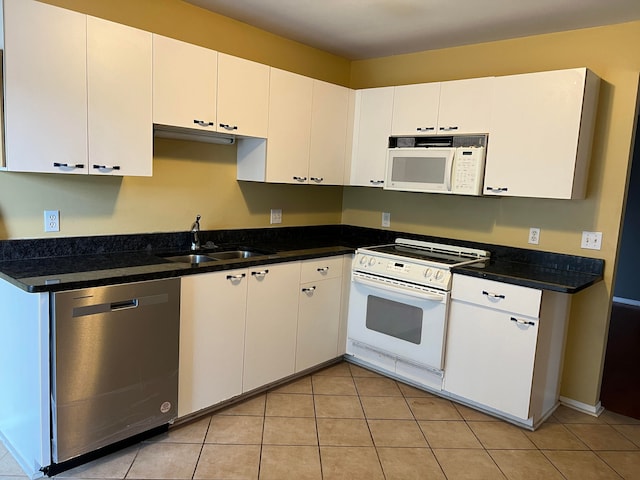 kitchen with white appliances, dark stone counters, sink, light tile patterned floors, and white cabinetry