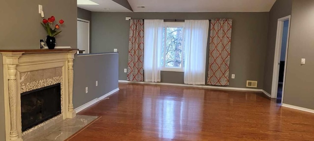 unfurnished living room with a tiled fireplace, wood-type flooring, and lofted ceiling