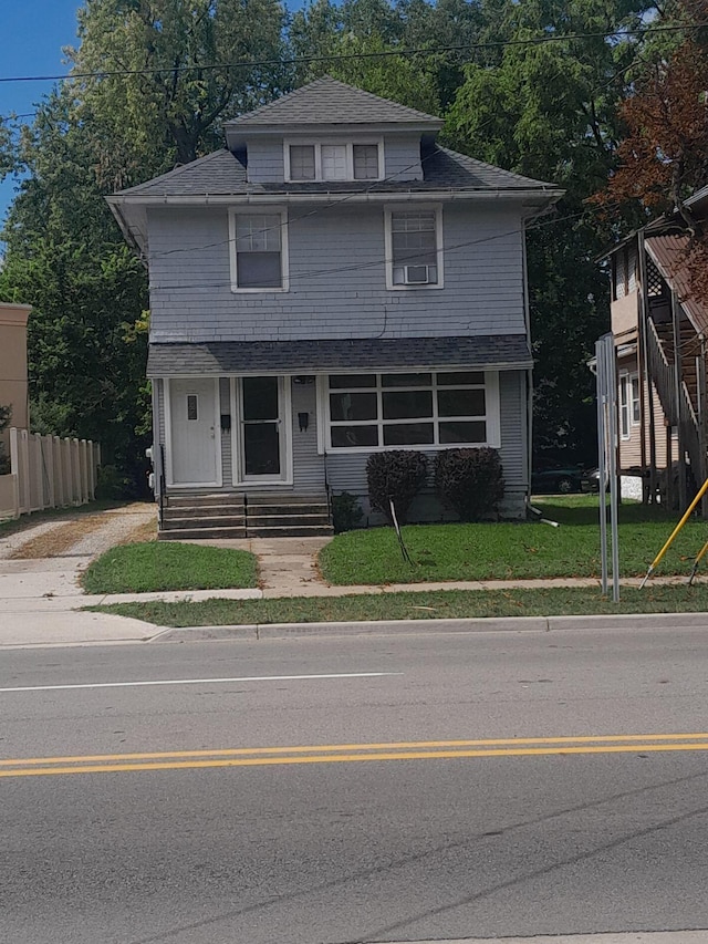 american foursquare style home featuring roof with shingles, a front yard, and fence