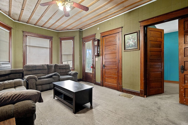 carpeted living room with ceiling fan, crown molding, and wooden walls