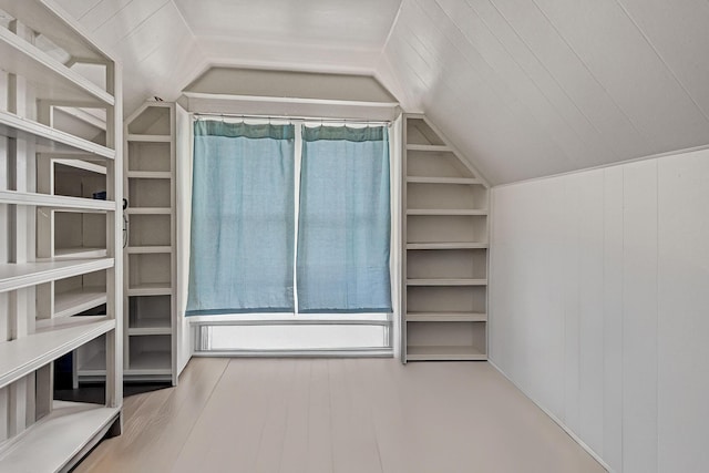 additional living space with built in shelves, wooden walls, lofted ceiling, and light wood-type flooring