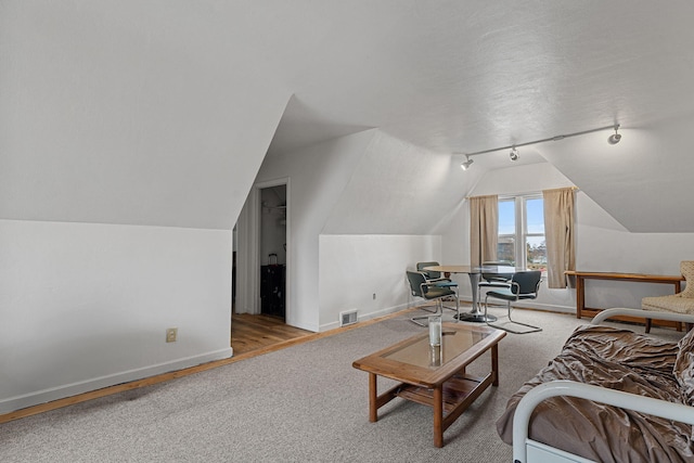 living room featuring a textured ceiling, rail lighting, light hardwood / wood-style flooring, and lofted ceiling