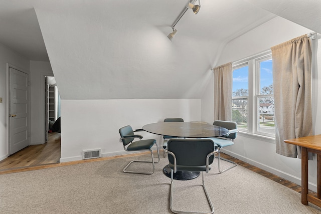 dining room with wood-type flooring, rail lighting, and vaulted ceiling