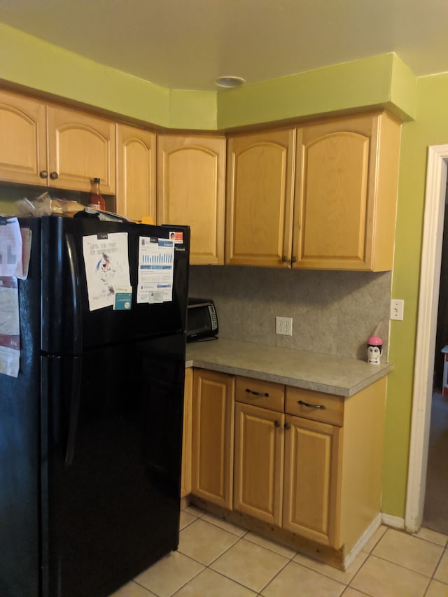 kitchen featuring light tile patterned floors, backsplash, black fridge, and light brown cabinetry