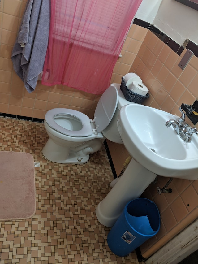 bathroom with sink, toilet, and tile walls