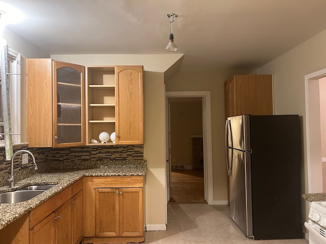 kitchen with stone counters, stainless steel fridge, backsplash, and sink