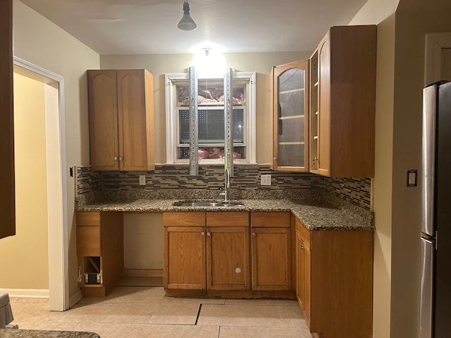 kitchen with backsplash, dark stone countertops, stainless steel fridge, and sink