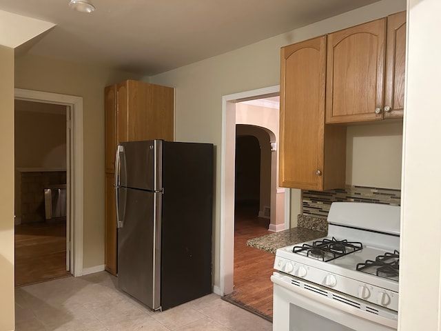 kitchen featuring light wood-type flooring, stainless steel fridge, white gas range oven, and light brown cabinetry