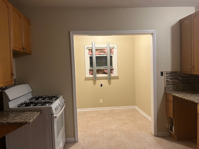 kitchen with dark stone countertops, gas range gas stove, and light tile patterned flooring