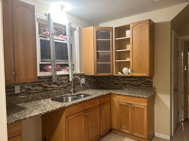 kitchen with backsplash, dark stone countertops, sink, and light tile patterned flooring