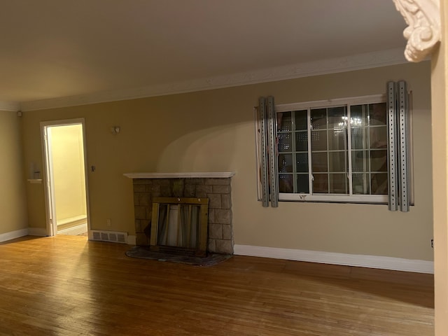 unfurnished living room featuring wood-type flooring, a stone fireplace, and ornamental molding