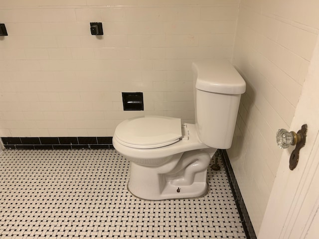 bathroom with toilet, tile patterned floors, and tile walls