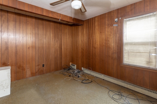 spare room with carpet, ceiling fan, wooden walls, and a baseboard radiator