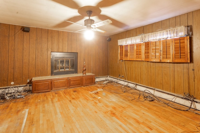 unfurnished living room featuring wood walls, wood-type flooring, and a baseboard heating unit