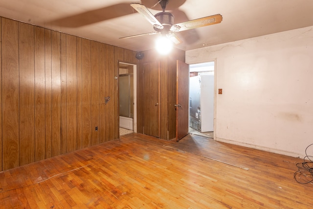 unfurnished room featuring ceiling fan, wooden walls, and light hardwood / wood-style flooring