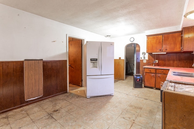 kitchen with a textured ceiling, sink, white fridge with ice dispenser, and wood walls