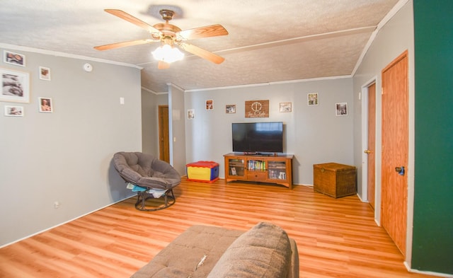 living room with ceiling fan, crown molding, light wood-type flooring, and a textured ceiling