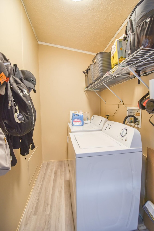 clothes washing area featuring light wood-type flooring, a textured ceiling, washing machine and dryer, and ornamental molding