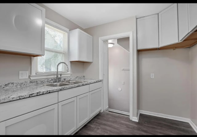 kitchen with light stone countertops, dark hardwood / wood-style flooring, white cabinetry, and sink