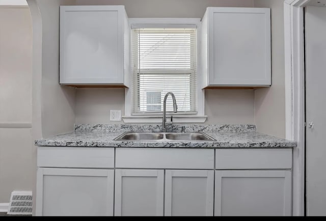 kitchen with white cabinets, light stone counters, and sink