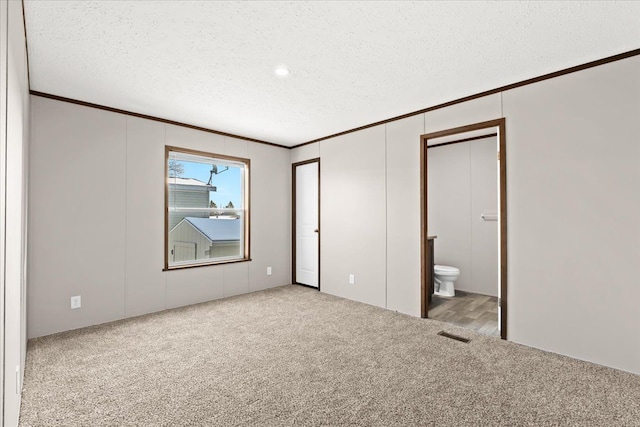 unfurnished bedroom with ensuite bathroom, light colored carpet, a textured ceiling, and crown molding