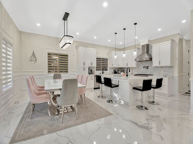 kitchen featuring decorative backsplash, wall chimney exhaust hood, decorative light fixtures, a center island with sink, and white cabinetry